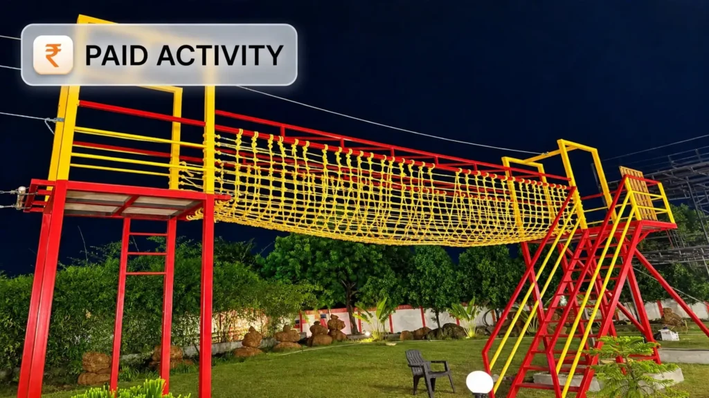 A vibrant yellow rope commando net crossing bridge illuminated at night for campers at My Adventure Zone in Ananthagiri Hills.