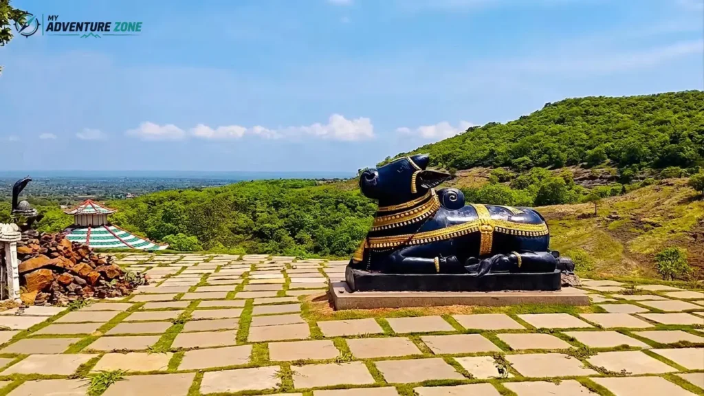 Polished black Nandi bull statue with gold ornaments on stone paved terrace at Ananthagiri Hills viewpoint